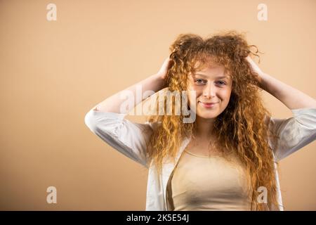 Ritratto di sorridente arrosshead bella giovane donna in posa per la fotocamera tenendo le mani sui capelli e li raddrizza. Foto Stock