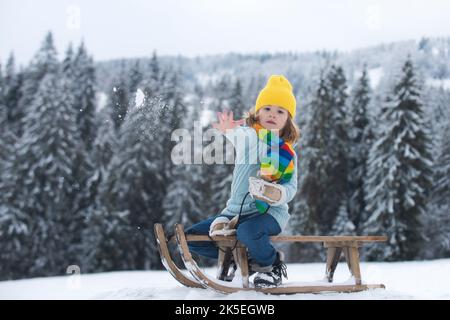 Bambino ragazzo slittando in inverno, giocando con la palla di neve. Bambini in inverno a cavallo sugli scivoli di neve. Inverno foresta di natale con neve caduta e alberi. Foto Stock