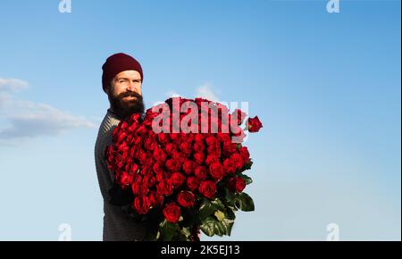 Uomo con bouquet di fiori. Happy man tiene un grande bouquet di rose rosse, proporre al fidanzato in data. Foto Stock