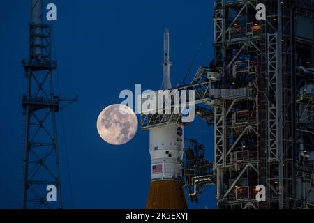 Una Luna piena è in vista dal Launch Complex 39B al Kennedy Space Center della NASA in Florida il 14 giugno 2022. Il sistema spaziale Artemis i Space Launch System (SLS) e la navicella spaziale Orion, in cima al lanciatore mobile, sono in preparazione per una prova di vestito bagnato per praticare le tempistiche e le procedure per il lancio. La prima di una serie sempre più complessa di missioni, Artemis i testerà SLS e Orion come sistema integrato prima dei voli con equipaggio per la Luna. Attraverso Artemis, la NASA atterrà la prima donna e la prima persona di colore sulla superficie lunare, spianando la strada ad una presenza lunare a lungo termine e utilizzando il Moo Foto Stock
