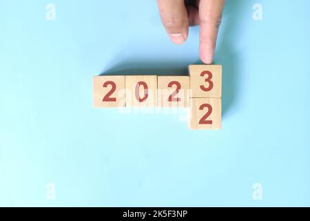 Cambio a mano anno 2022 a 2023 in blocchi di legno cubetti su sfondo blu. Anno nuovo 2023, Hope, Hello e Arrivederci Concept. Foto Stock