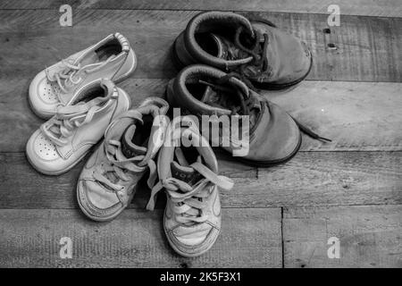 Tre paia di scarpe per bambini su un pavimento in legno duro in bianco e nero Foto Stock