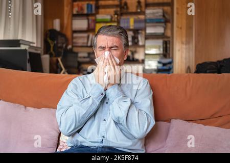 Malato di influenza e starnuti in un tessuto, seduto a casa. Foto Stock
