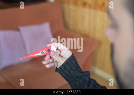 Uomo malato che guarda l'alta temperatura marcata sul termometro dopo essersi verificato. Foto Stock