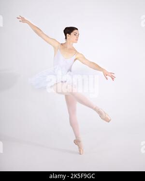 Perso nella danza. Ballerina giovane dedicata che balla en pointe su sfondo bianco. Foto Stock