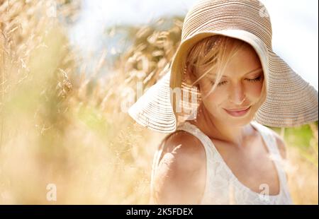 È una giornata così bella...una bella giovane donna in un cappello da sole che cammina attraverso erba alta. Foto Stock