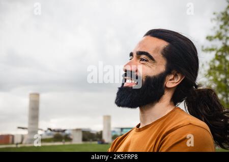 Felice uomo bearded con i capelli lunghi che si divertono sorridendo in un parco Foto Stock