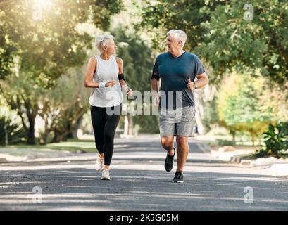 Salute, coppia anziana e corsa mentre si parla e si esercita per fitness, benessere e sano insieme in natura. La pensione, l'uomo e la donna godono Foto Stock