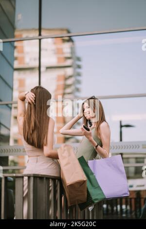 Due ragazze graziose in piedi vicino al recinto mentre una di loro sta toccando i suoi capelli Foto Stock