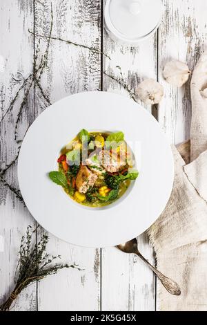 Vista dall'alto appetitose polpette di pesce con brodo. Servito su un piatto bianco. Cotoletta di salmone con zuppa di pesce e verdure. Sfondo bianco legno. Verticale Foto Stock