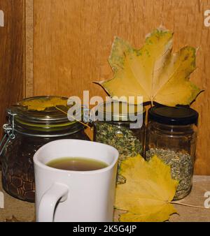 Bottiglie di vetro con caffè macinato e tè con foglie gialle. Sul tavolo con una tazza bianca di tè. Foto Stock