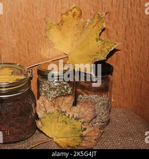 Bottiglie di vetro con caffè macinato e tè con foglie gialle. Sul tavolo. Foto Stock