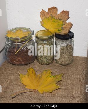 Bottiglie di vetro con caffè macinato e tè con foglie gialle. Sul tavolo. Foto Stock