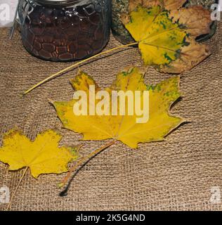 Bottiglie di vetro con caffè macinato e tè con foglie gialle. Sul tavolo. Autunno. Foto Stock