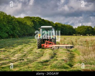 Un trattore agricolo che esegue operazioni di insilaggio in un campo erboso nel Kent, Inghilterra, Regno Unito Foto Stock