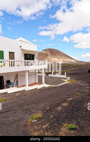 Tipica casa colonica bianca delle Canarie sull'isola di Lanzarote a Mancha Blanca con crateri vulcanici sullo sfondo in un soleggiato pomeriggio invernale. Lanzarote è Foto Stock