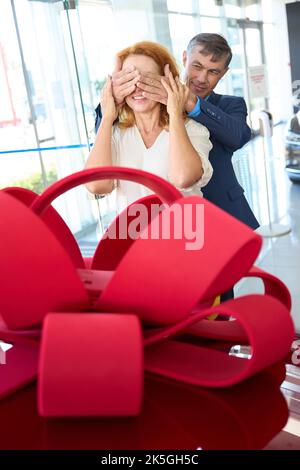 L'uomo chiuse gli occhi della donna, le palme, gli dà la macchina rossa Foto Stock