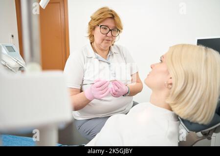 Donna dentista in occhiali comunica con un paziente Foto Stock