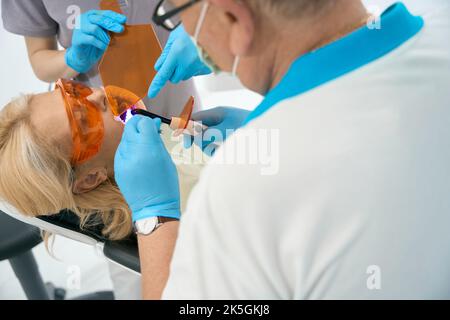 Donna che riceve cure odontoiatriche con lampada di polimerizzazione in clinica medica Foto Stock