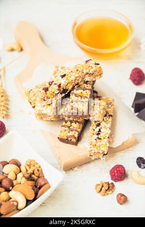 Vari barrette di muesli fatti in casa con noci, semi, cioccolato fondente, miele e bacche su un asse di legno. Foto Stock