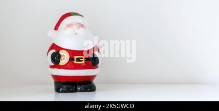 Sfondo a tema di Natale di statuetta Babbo Natale in piedi inclinato di fronte a destra dove c'è un sacco di spazio copia Foto Stock