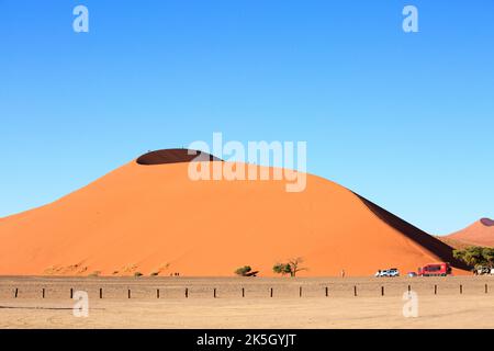 Dune 45 nel deserto del Namib con persone che si arrampicano. C'è un parcheggio sotto la duna dove i turisti possono parcheggiare e riposarsi. Foto Stock