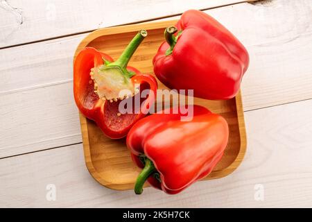 Due peperoni rossi interi e mezzo su un piatto di bambù, primo piano, su un tavolo di legno, vista dall'alto. Foto Stock