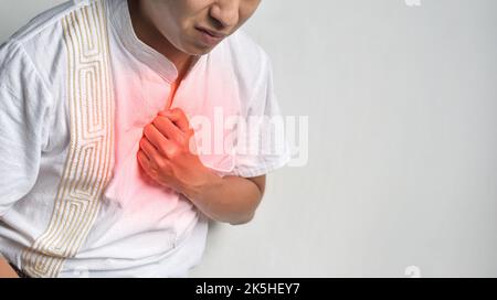 Giovane asiatico che soffre di dolore al torace centrale. Il dolore toracico può essere causato da attacco cardiaco, infarto miocardico o ischemia, miocardite, polmonite, o Foto Stock