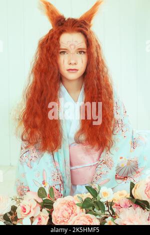 giovane ragazza dai capelli rossi con orecchie e code volpe. Nove volpe a coda. Ragazza giovane in kimono Foto Stock