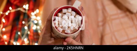 tazza di cioccolata calda o caffè con marshmallows in femmina tenendo le mani sulle gambe di donna in maglia maglione rilassante e godendo il holida Foto Stock