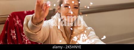 giovane donna sfuocata che tiene in mano sparklers bengala fuoco bastoni seduta sedia con la tela rossa all'aperto su felice anno nuovo e buon natale wi Foto Stock