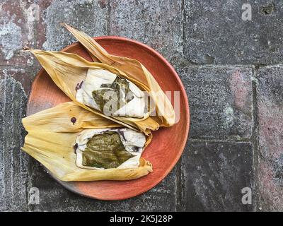 Due tamales di Oaxacan su un piatto di argilla fatto con hoja babbo natale e riempito di fagioli Foto Stock