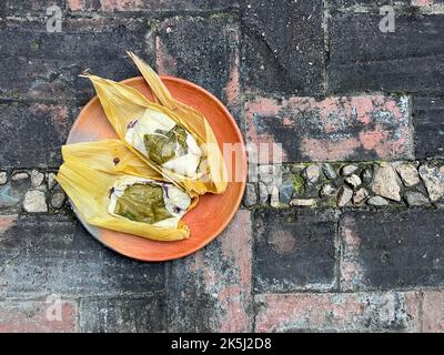 Due tamales di Oaxacan su un piatto di argilla fatto con hoja babbo natale e riempito di fagioli Foto Stock