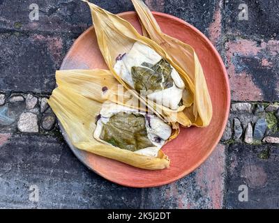 Due tamales di Oaxacan su un piatto di argilla fatto con hoja babbo natale e riempito di fagioli Foto Stock