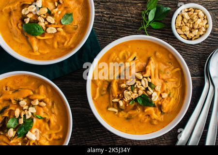 Zuppa di noodle piccante di zucca al curry tailandese guarnita con arachidi e basilico tailandese: Zuppa spessa o stufato a base di zucca, tagliatelle di riso e funghi shiitake Foto Stock