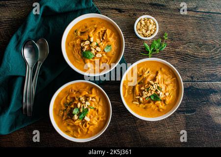 Zuppa di noodle piccante di zucca al curry tailandese guarnita con arachidi e basilico tailandese: Zuppa spessa o stufato a base di zucca, tagliatelle di riso e funghi shiitake Foto Stock