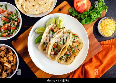 Taco di pollo con Pico de Gallo e formaggio: Tre Taco su un piatto circondato da condimenti e tortillas Foto Stock