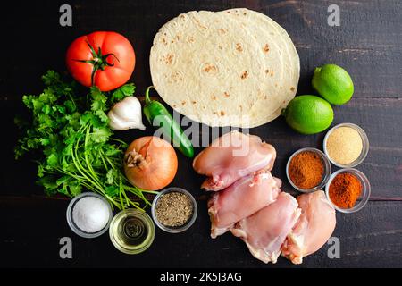 Ingredienti crudi per taco di pollo alla griglia con condimenti: Cosce di pollo, tortillas di farina e altri ingredienti di taco visti dall'alto Foto Stock