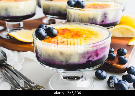 Mirtillo-arancia Creme Brulee guarnito con mirtilli freschi: Vista laterale della crema su confettura di mirtilli ricoperta di zucchero caramellato Foto Stock