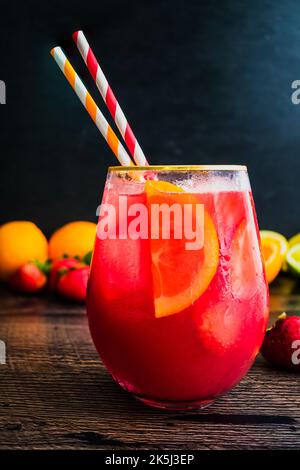 Punch di rum Arancio al sangue di fragole con garze e cannucce di carta: Cocktail al rum preparato con frutta fresca servito su cubetti di ghiaccio Foto Stock