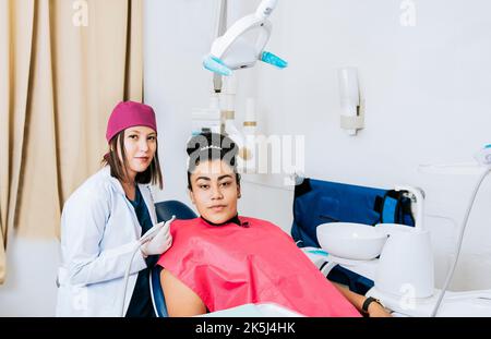 Ritratto di giovane dentista con paziente femmina in ufficio medico, dentista femmina con paziente femmina che guarda la macchina fotografica, dentista professionista con Foto Stock
