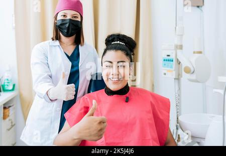 Dentista femminile con paziente soddisfatto sorridente alla telecamera e che dà il pollice in su, dentista femminile con paziente sorridente e che dà il pollice in su. Ritratto di Foto Stock