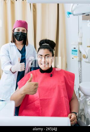Dentista con paziente sorridente e che dà pollice in su. Dentista femminile con paziente soddisfatto sorridente alla telecamera e dando pollice in su, Ritratto della femmina Foto Stock