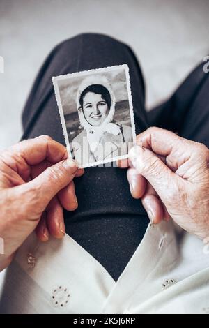 CIRCA 1970: Donna anziana mani in possesso di vintage, foto in bianco e nero della giovane donna. Il concetto di passare del tempo Foto Stock