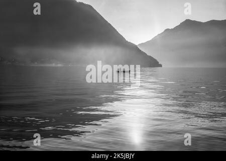 Idilliaco paesaggio sul lago di Como (un po 'di nebbia) con barca di fishier e piccolo corpo di pescatore a distanza (persona irriconoscibile) la settimana di Natale in Foto Stock