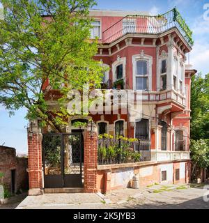 Facciata esterna di un vecchio edificio residenziale rosso, con finestre in ferro battuto, balconi e alberi verdi, quartiere Balat, Istanbul, Turchia Foto Stock