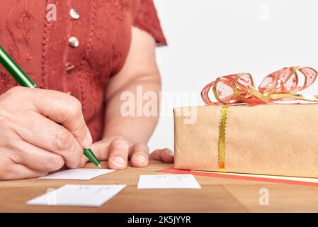 Donna matura irriconoscibile che scrive, facendo le schede fatte a mano per mettere sui suoi regali di Natale. Design semplice con spazio di copia. Foto Stock