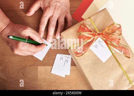 Donna matura irriconoscibile che scrive, facendo le schede fatte a mano per mettere sui suoi regali di Natale. Composizione vista dall'alto con spazio di copia. Foto Stock