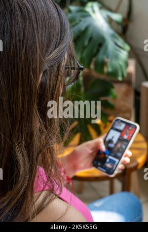 Felice millenario ispanica ragazza teenager controllare i social media tenendo smartphone a casa. Foto Stock