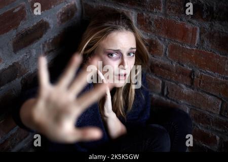 Per favore, non. La giovane donna ha abusato accovacciato e accovacciato in un angolo mentre si allunga in un gesto di arresto. Foto Stock